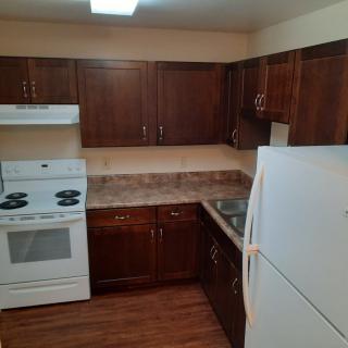 A kitchen with dark wooden cabinets, a white stove and refrigerator, and a tiled countertop.