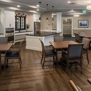 A modern kitchen and dining area with wood flooring, featuring tables and chairs under pendant lighting.