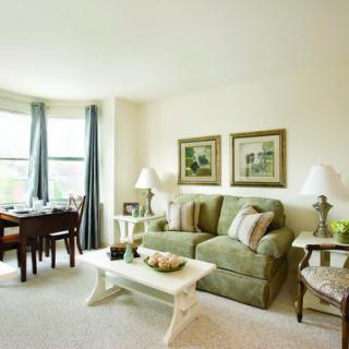 A cozy living room with a green sofa, white coffee table, and dining area by the window.