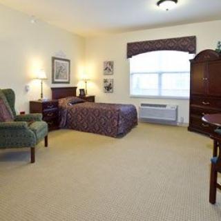 A cozy bedroom with a bed, armchair, lamps, and a large window.