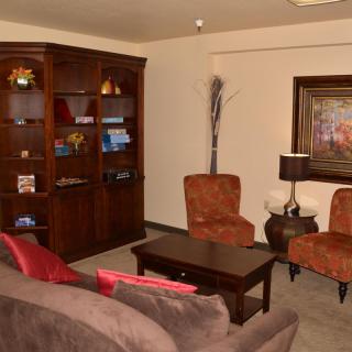A cozy living room with a bookshelf, chairs, sofa, and table.