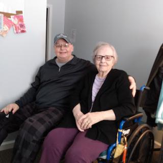 A warm moment shared between two seniors, one seated in a wheelchair, enjoying each other's company.
