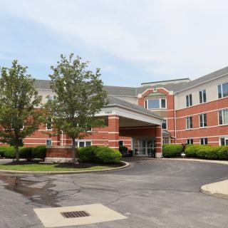 A view of a hotel exterior with a driveway and surrounding trees.