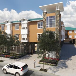 A modern apartment building with a parking area and surrounding trees under a clear sky.