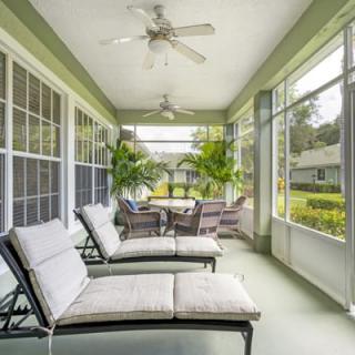 A bright sunroom featuring comfortable lounge chairs and a table, surrounded by large windows and lush plants.