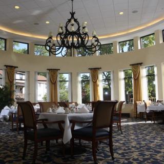 An elegant restaurant dining room featuring a large chandelier and tall windows.