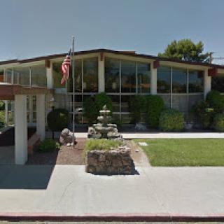 A modern building featuring large glass windows and a landscaped entrance with a fountain and an American flag.