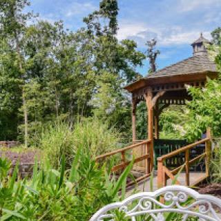 A serene view of a wooden gazebo nestled in a lush garden surrounded by trees.