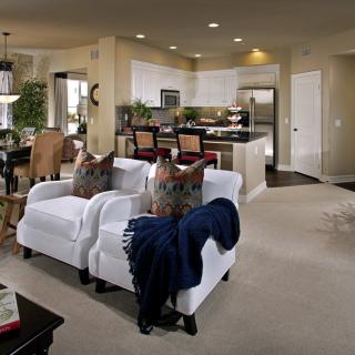 A cozy open living room area with white armchairs and a view of the kitchen.