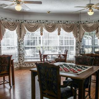 A cozy living area with elegant curtains, wooden tables and chairs, and ceiling fans.