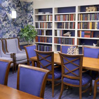 A cozy library room with bookshelves, a large table, and comfortable chairs.