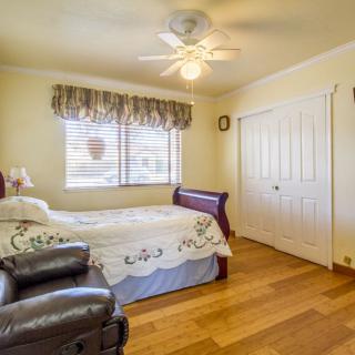 A cozy bedroom with a bed, wooden flooring, and a ceiling fan.