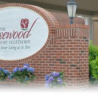 A brick wall with a sign for 'The Rosewood,' featuring flowers and a lamp post.