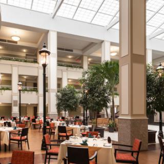 A spacious and elegantly designed restaurant featuring a glass ceiling, inviting tables, and greenery.