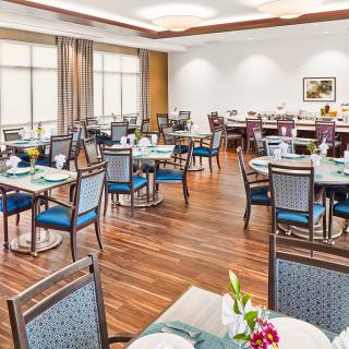 A well-lit dining area with neatly arranged tables and chairs, featuring a wooden floor and elegant decor.