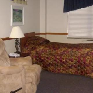 A cozy bedroom with a single bed, a lamp on a side table, and an armchair.