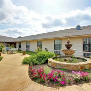 A serene courtyard with a central fountain, surrounded by colorful flowers and a paved pathway.