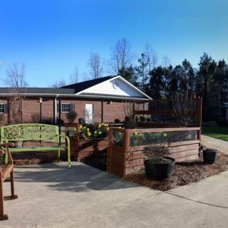 An outdoor area with benches and a garden in front of a brick building under a clear blue sky.