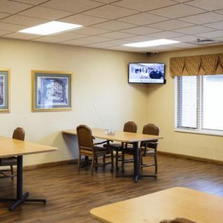 A small cafeteria with tables and chairs, a TV on the wall, and artwork hanging on the walls.