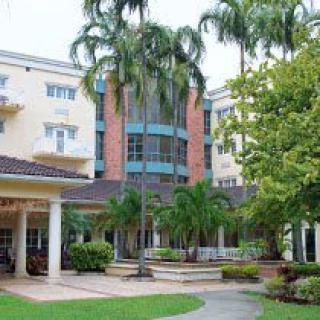A multi-story building surrounded by palm trees and landscaped gardens.
