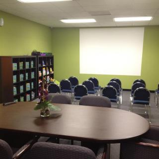 A meeting room with a projector screen, chairs arranged in rows, and bookshelves along the wall.