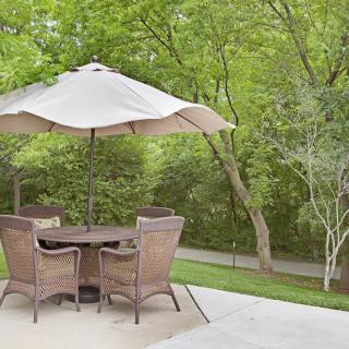 A peaceful patio setup with a table, chairs, and an umbrella surrounded by lush greenery.