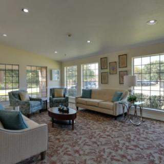 A cozy living room with large windows, sofas, and armchairs arranged around a central coffee table.
