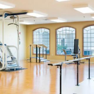 A spacious rehabilitation center with various gym equipment and parallel bars for physical therapy exercises.