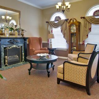 A traditional-style living room with elegant furnishings, featuring a fireplace, armchairs, and a grandfather clock.