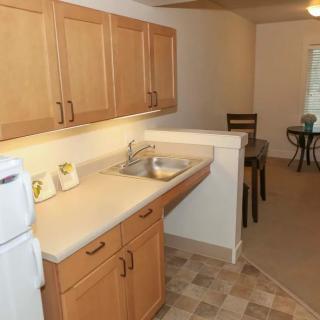 A compact kitchen with wooden cabinets and a small dining area in the background.