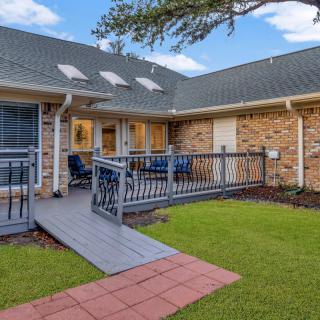 A charming brick house with a ramp leading to a cozy patio and well-maintained yard.