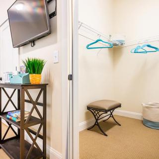 A neatly organized closet space with hangers and a bench next to a TV stand in a well-decorated room.