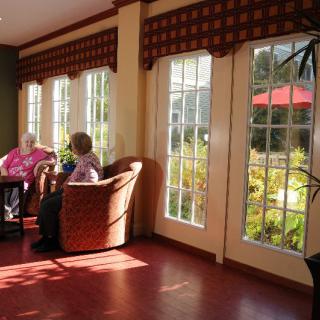 Two people seated in a sunlit room, enjoying a conversation by large windows.
