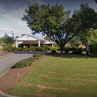 A peaceful suburban scene featuring a large tree and a well-maintained building along a winding road.