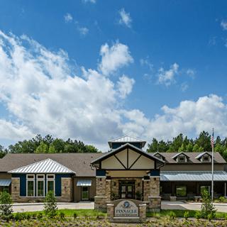 A modern building surrounded by greenery under a bright blue sky with clouds.