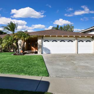 A charming suburban home with a spacious front yard and a three-car garage under a bright blue sky.