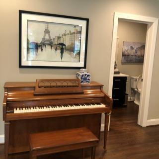 A cozy living room with a piano and artwork adorning the walls.