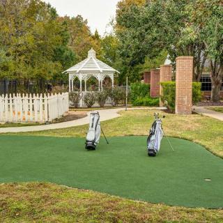 A serene outdoor setting featuring a small putting green with two golf bags, surrounded by trees and a gazebo.
