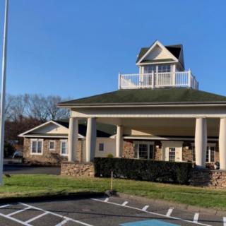 A building with a prominent covered entrance and columns in front of a parking lot under a clear blue sky.