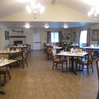 An empty dining room with neatly set tables and chairs, illuminated by overhead lighting.