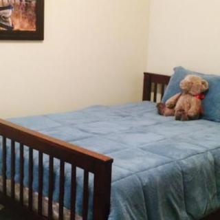 A cozy bedroom with a wooden bed, blue bedding, and a teddy bear sitting on top.