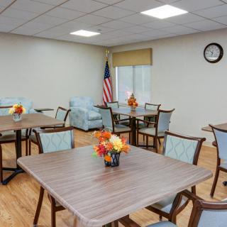 An empty dining room with tables and chairs, featuring floral centerpieces and an American flag in the corner.