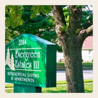 Sign for Evergreen Estates III Residential Living & Apartments next to a tree.