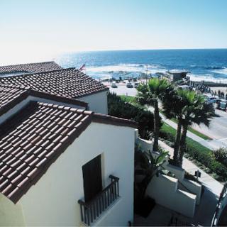 A picturesque coastal view featuring a charming house overlooking the ocean, surrounded by palm trees and clear blue skies.