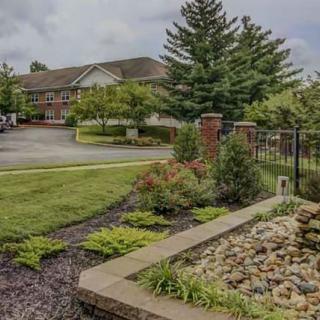 A well-maintained garden with a building in the background, featuring trees, grass, and a stone walkway.