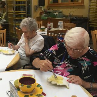 Two elderly women engaged in a painting activity at a table indoors.