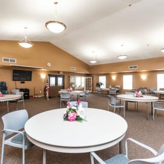 A spacious dining area with round tables and chairs, decorated with floral centerpieces.