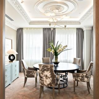 An elegantly designed dining room featuring a round table, plush upholstered chairs, and a striking chandelier overhead.