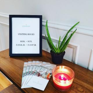 A welcoming setup features a framed sign, a small potted plant, a lit candle, and brochures arranged neatly on a table.