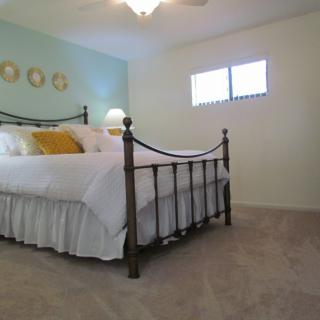 A cozy bedroom featuring a metal-framed bed with white bedding and yellow accent pillows, complemented by a soft carpet and warm lighting.